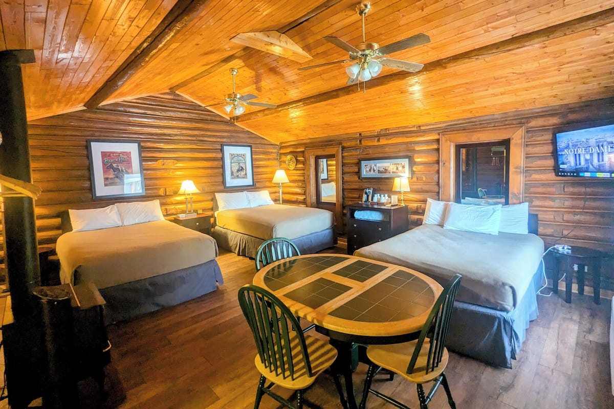 A log cabin-style room with two beds, a dining table, chairs, and ceiling fans.