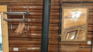 A wood-burning stove with a chimney, a mirror, and a fan in a wooden cabin. - Teton Court Motel (Pinedale)