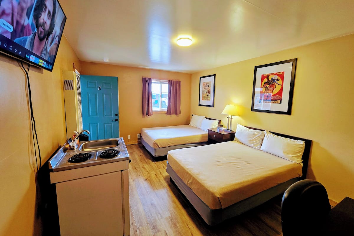 A hotel room with two beds, a kitchenette, a TV, and a poster on the wall.