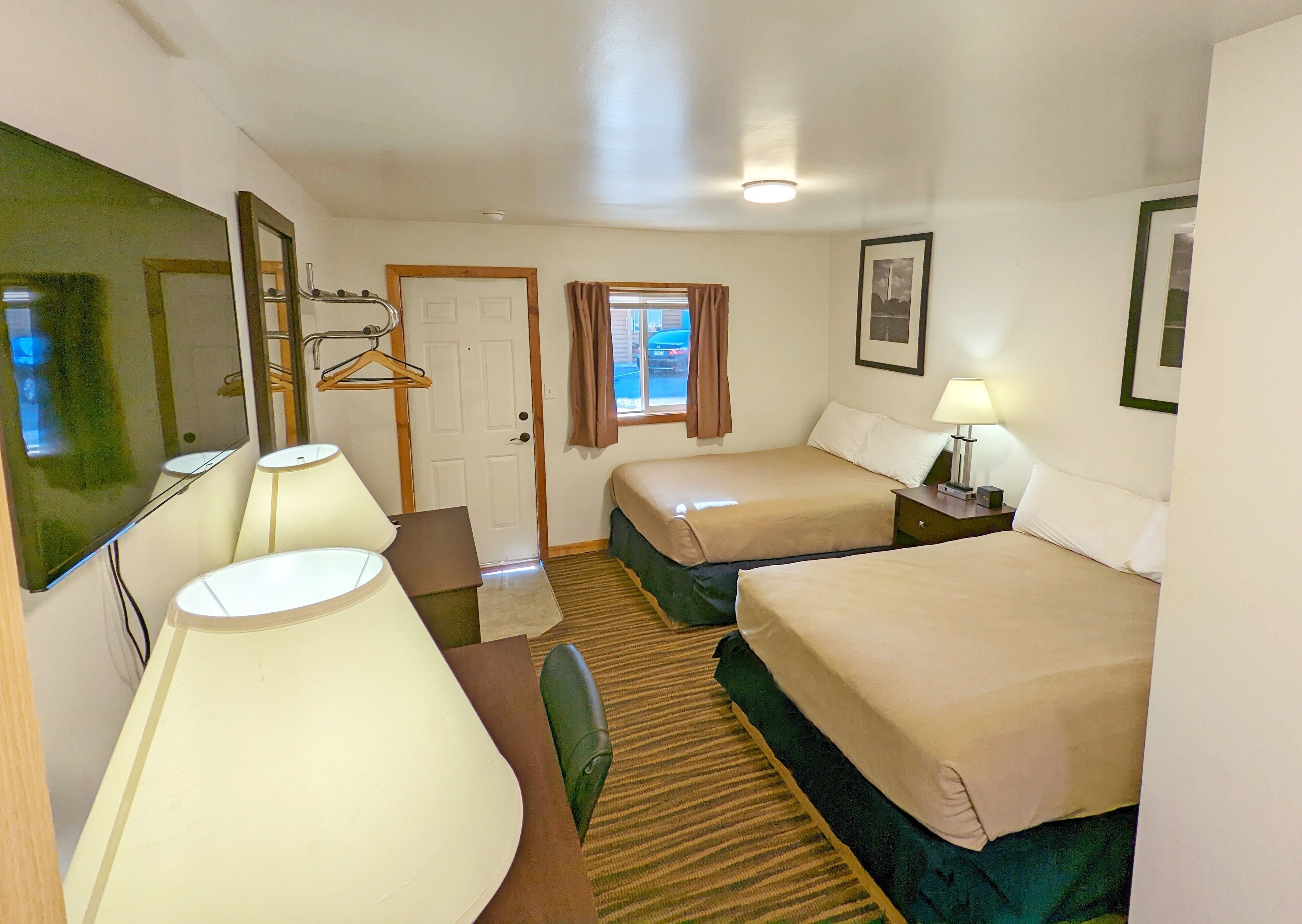 Habitación de hotel con dos camas, un escritorio, una silla, un espejo, una puerta y una ventana con cortinas.