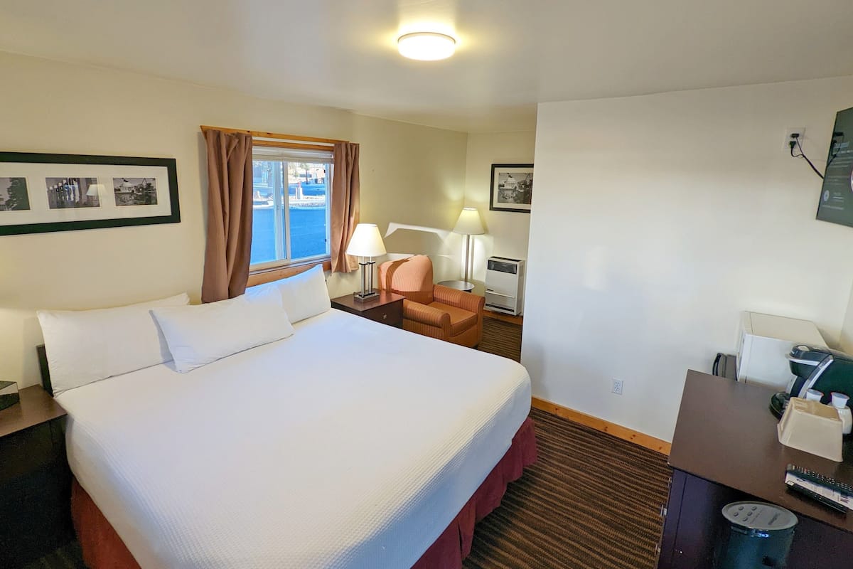 A hotel room with a large bed, a desk with a chair, a lamp, and a window with curtains.