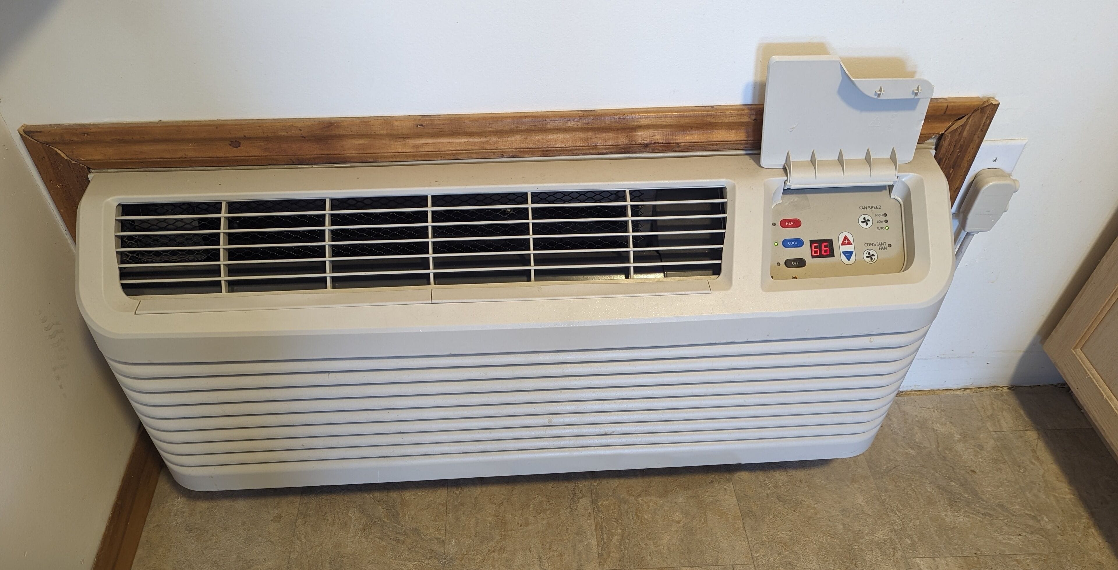 A white portable air conditioner with a control panel, placed against a wall with a wooden trim.