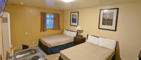 Habitación de hotel con dos camas, un kitchenette, una ventana con cortinas y cuadros en las paredes.