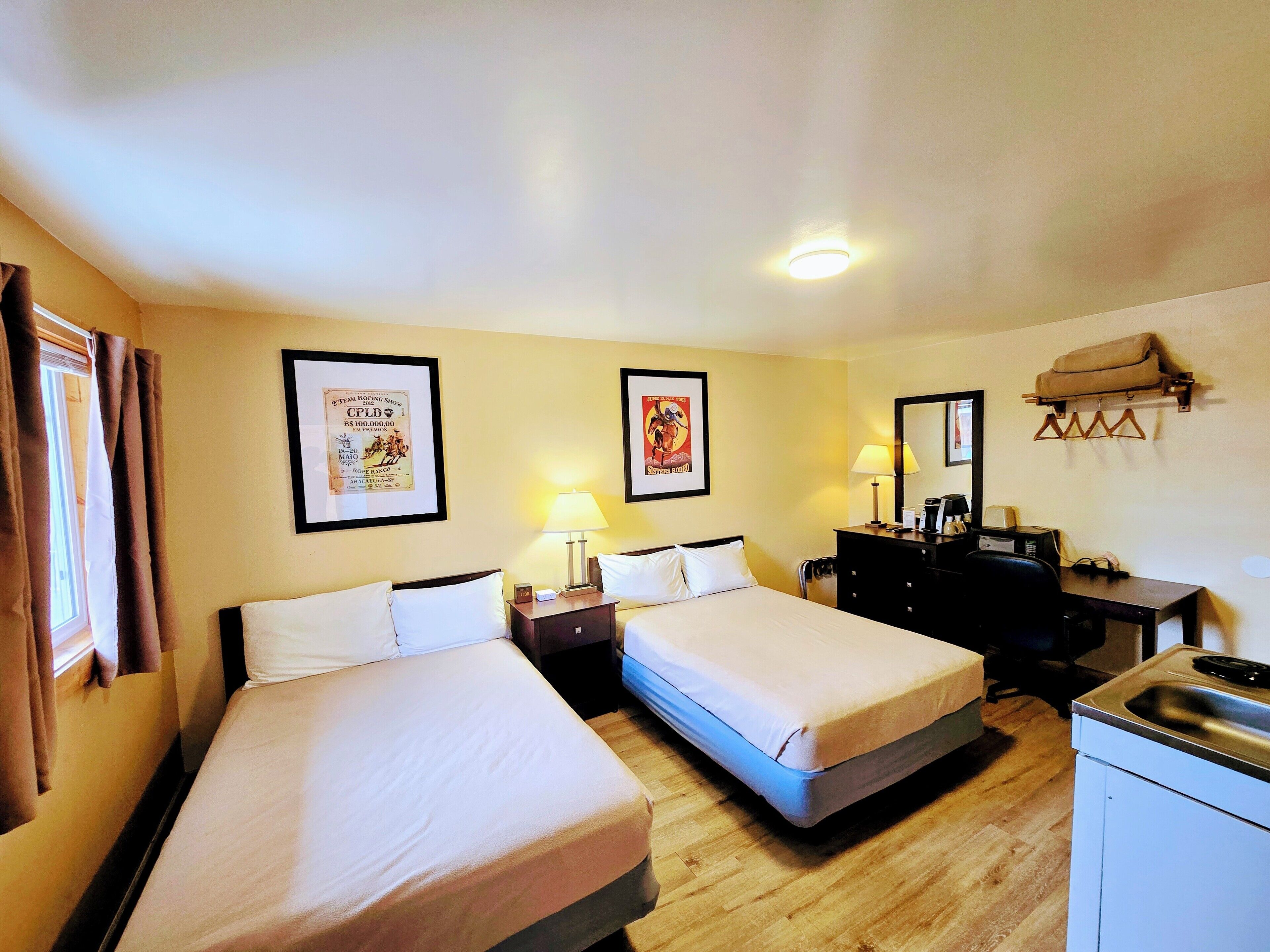 A hotel room with two beds, a desk, a dresser, a mirror, and a small kitchenette.