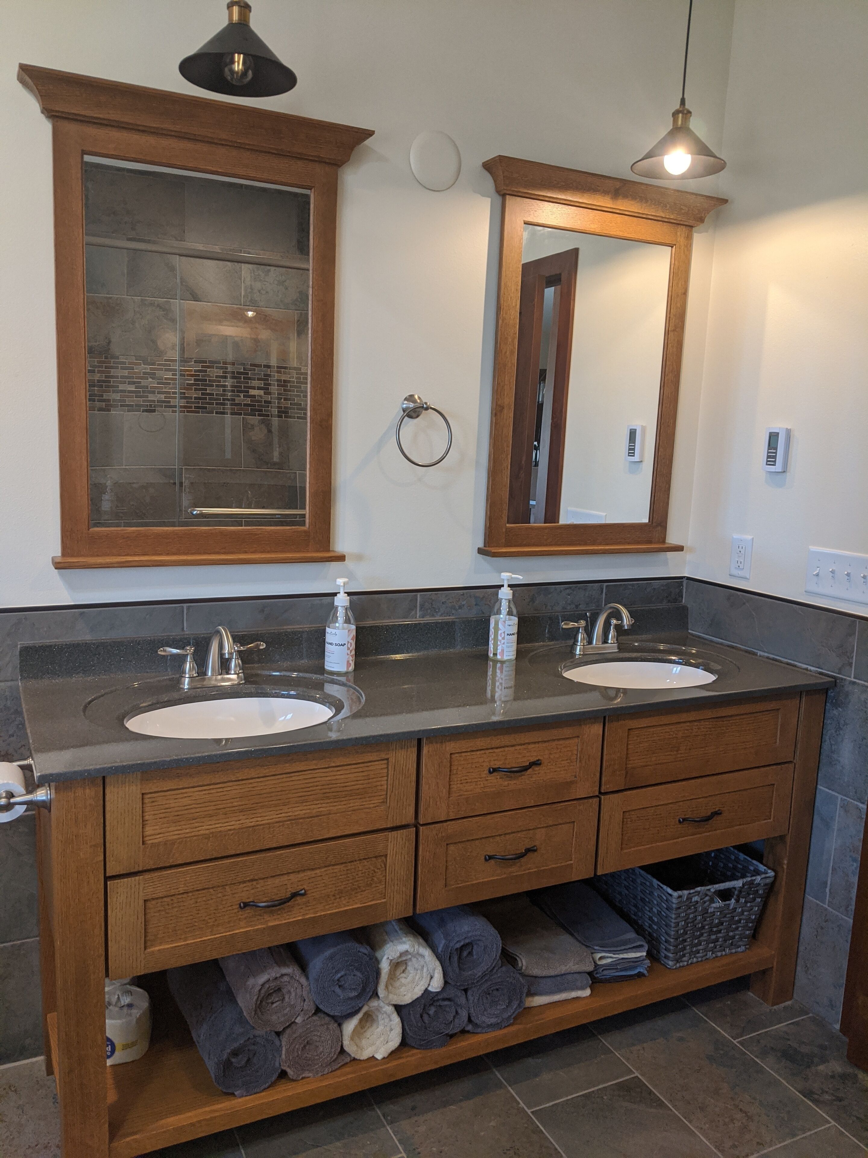 Baño con dos lavamanos, tocador de madera, espacio para toallas y un espejo.