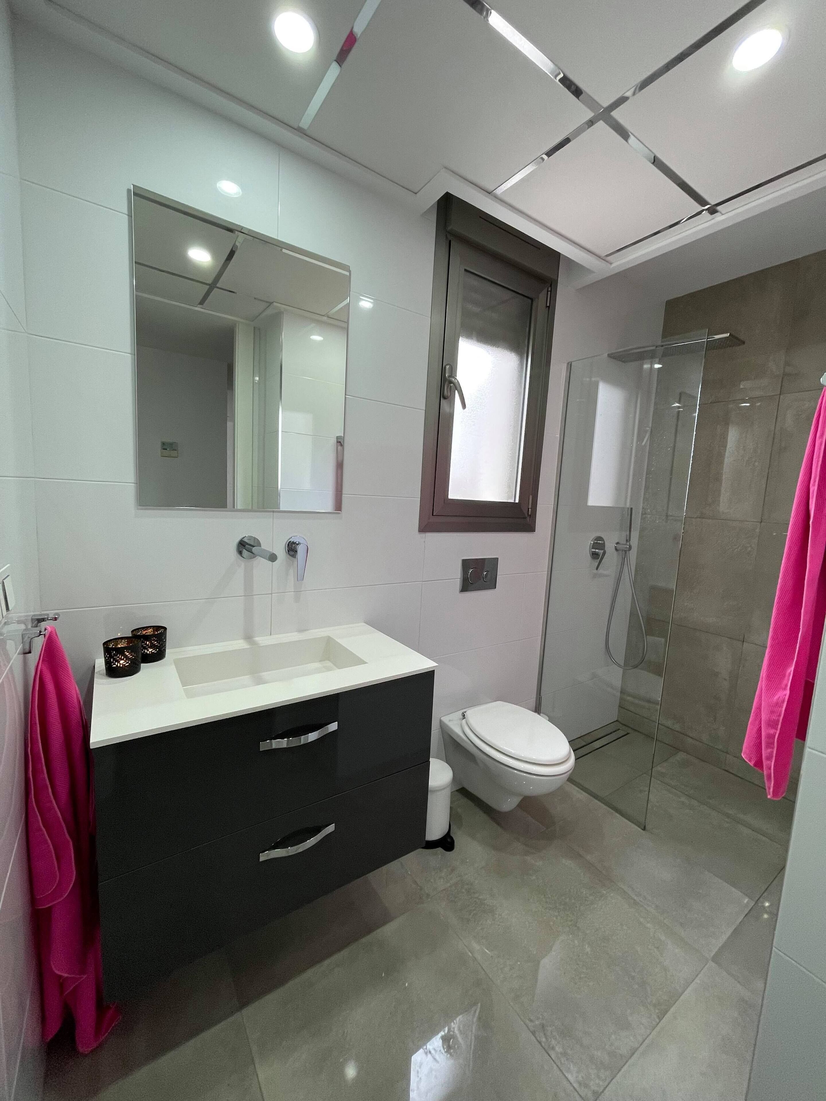 Een moderne badkamer met een wit badkamermeubel, een douchecabine van glas en een toilet.