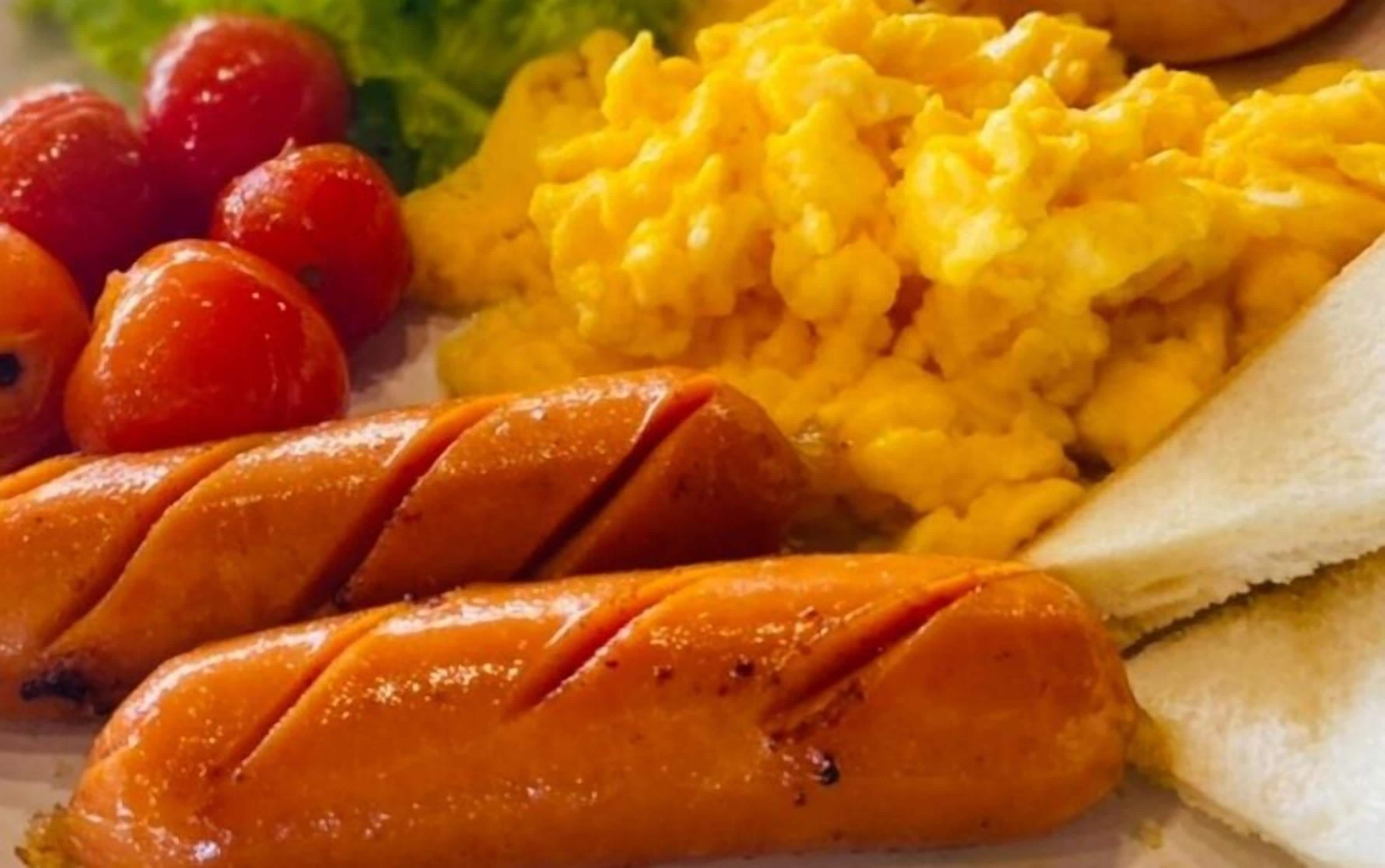 Une assiette avec des saucisses, des œufs brouillés et une tranche de pain.