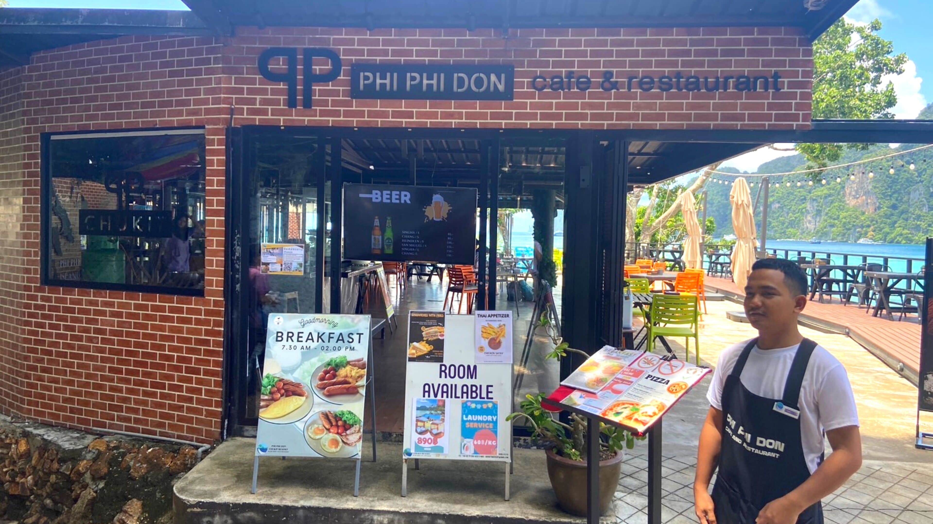A brick building with a sign reading "PHI PHI DON cafe & restaurant". There are signs for breakfast, room availability, and laundry service.