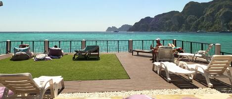 A deck with outdoor seating, a view of the sea, and a mountainous backdrop.