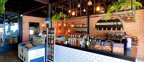 A bar area with a brick wall, shelves of beverages, and a counter with a beverage dispenser.