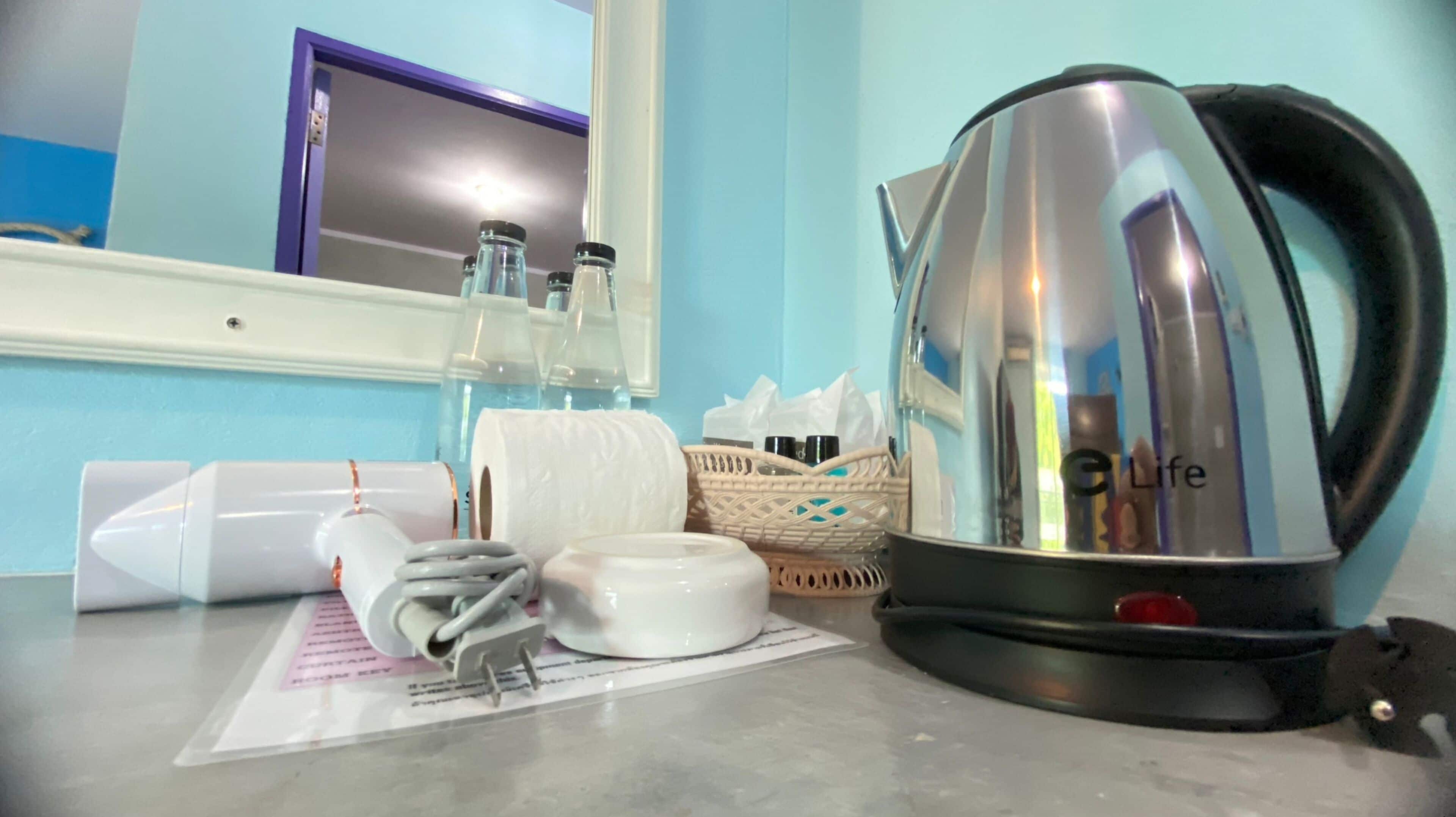 A kitchen counter with a kettle, a roll of paper towels, and a basket of toiletries.
