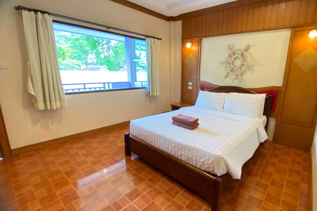 Une chambre d’hôtel avec un lit, une fenêtre avec des rideaux, une tête de lit en bois et une décoration murale représentant un gouvernail de bateau.
