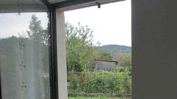 Ein Zimmer mit großem Fenster und Blick auf einen Garten sowie ein Gebäude in der Ferne.