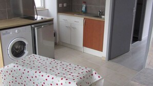 Eine kompakte Küche mit Waschmaschine, Mikrowelle und einem Tisch mit Kirschmuster-Tischdecke.