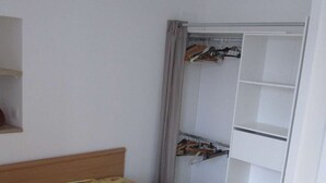 Ein Schlafzimmer mit einem Bett, einem Kleiderschrank mit Platz zum Aufhängen und einem Regal.