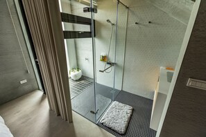A modern bathroom with a glass shower enclosure, a white sink, and a small rug on the floor.