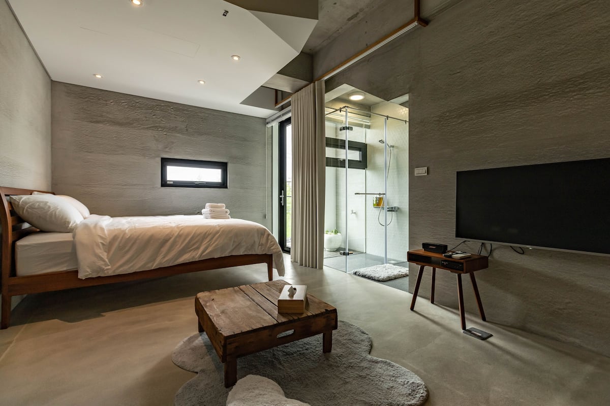 A modern bedroom with a bed, a TV, a coffee table, and a shower area.