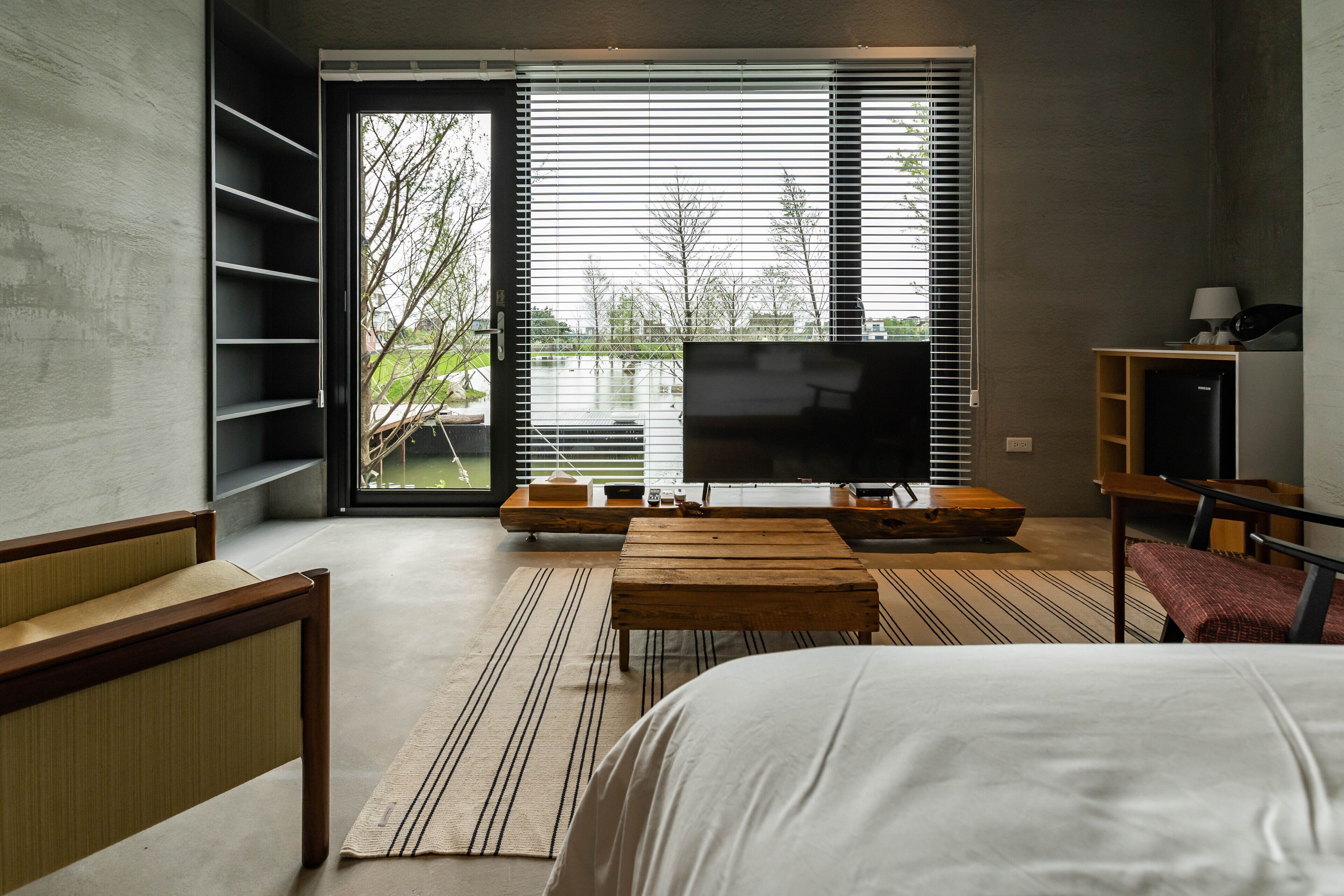 Ein modernes Schlafzimmer mit einem großen Bett, einem Fernseher und Blick auf einen See durch das Fenster.