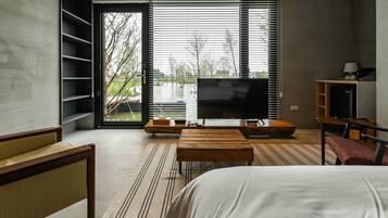 Ein modernes Schlafzimmer mit einem großen Bett, einem Fernseher und Blick auf einen See durch das Fenster.