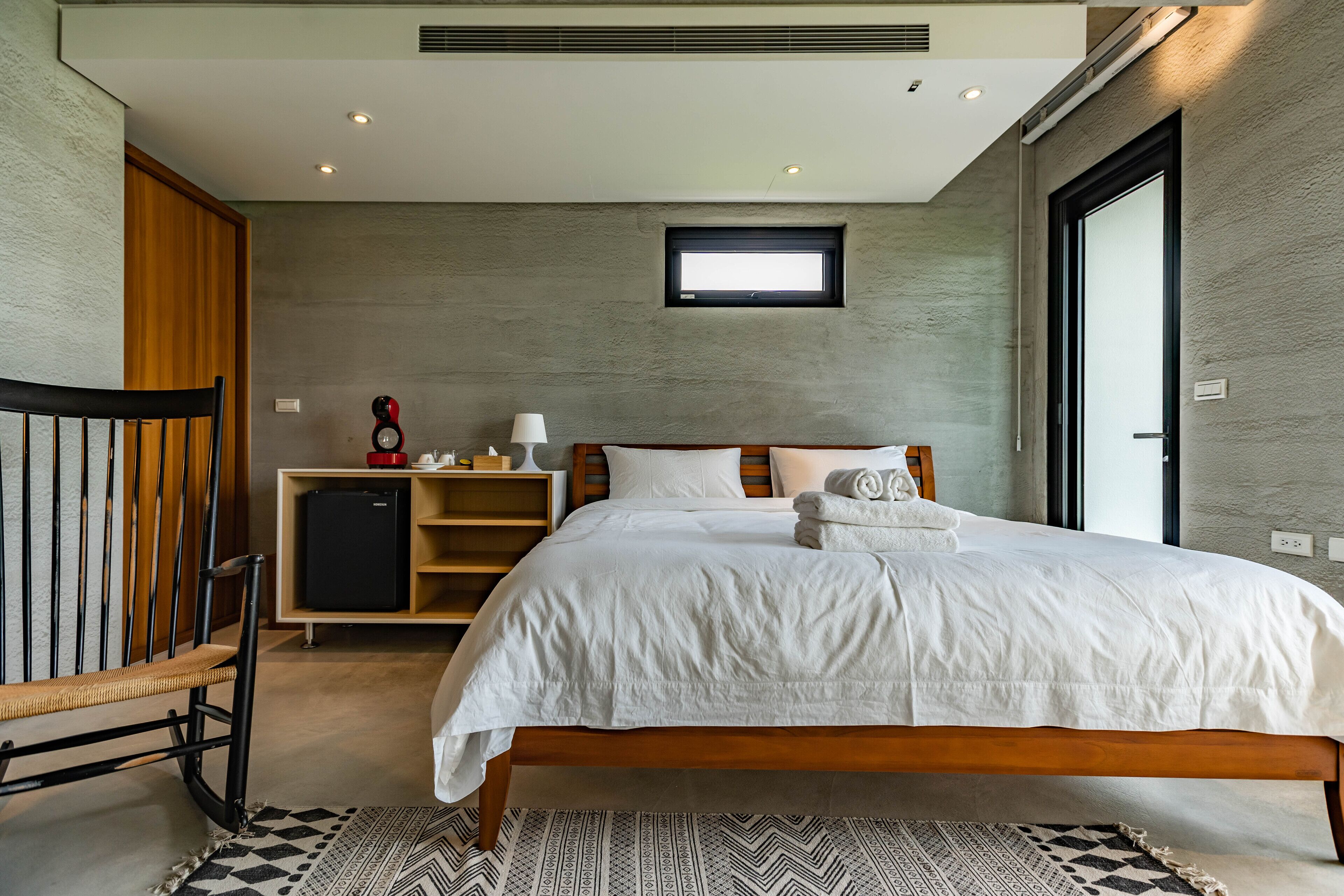 Een moderne slaapkamer met een houten bed, een klein bureau met een lamp en een garderobe.