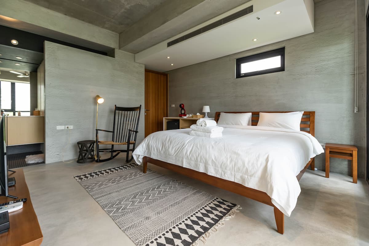A modern bedroom with a large bed, a wooden chair, a small table, and a floor lamp.