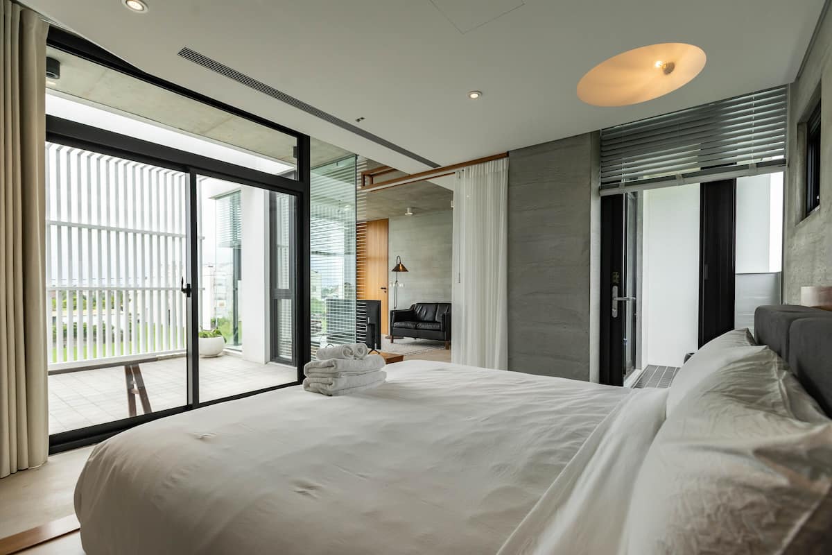 A modern hotel room with a large bed, sliding glass doors to a balcony, a sofa, and a desk.