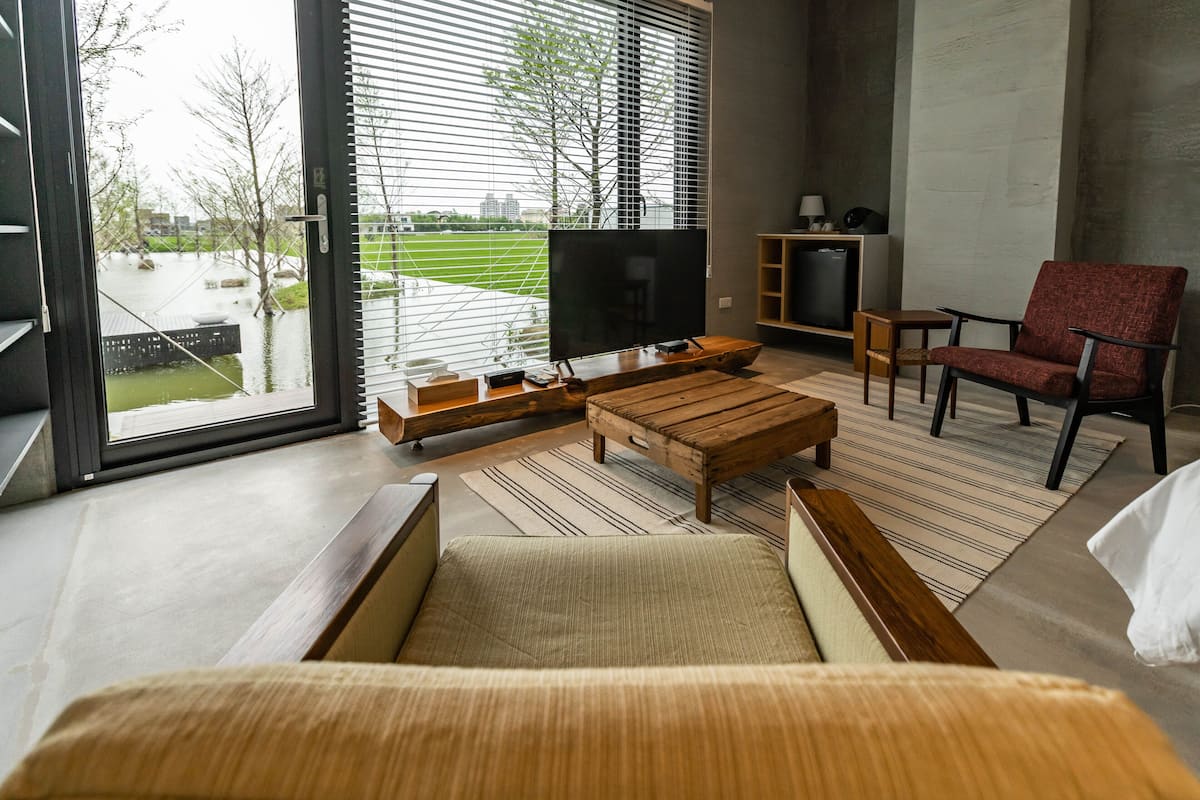 A modern living room with a large TV, wooden furniture, and a view of a park through large windows.