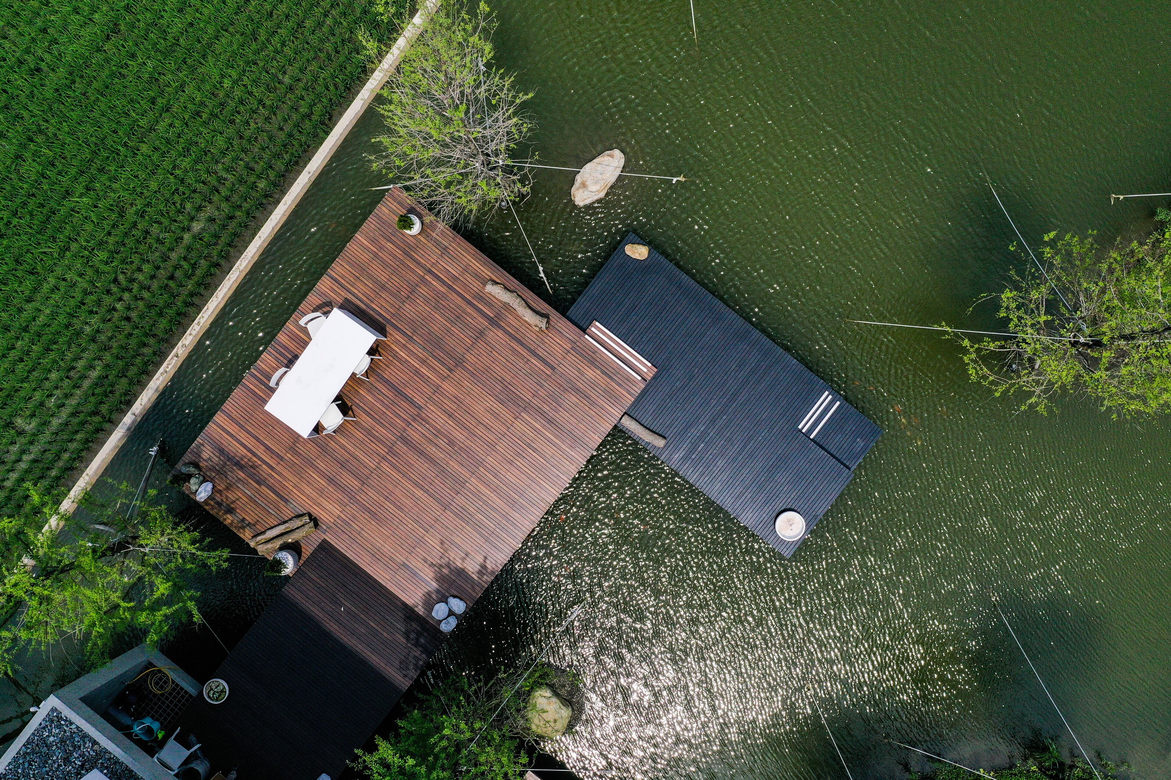 An aerial view of a dock extending into a lake, surrounded by greenery.
