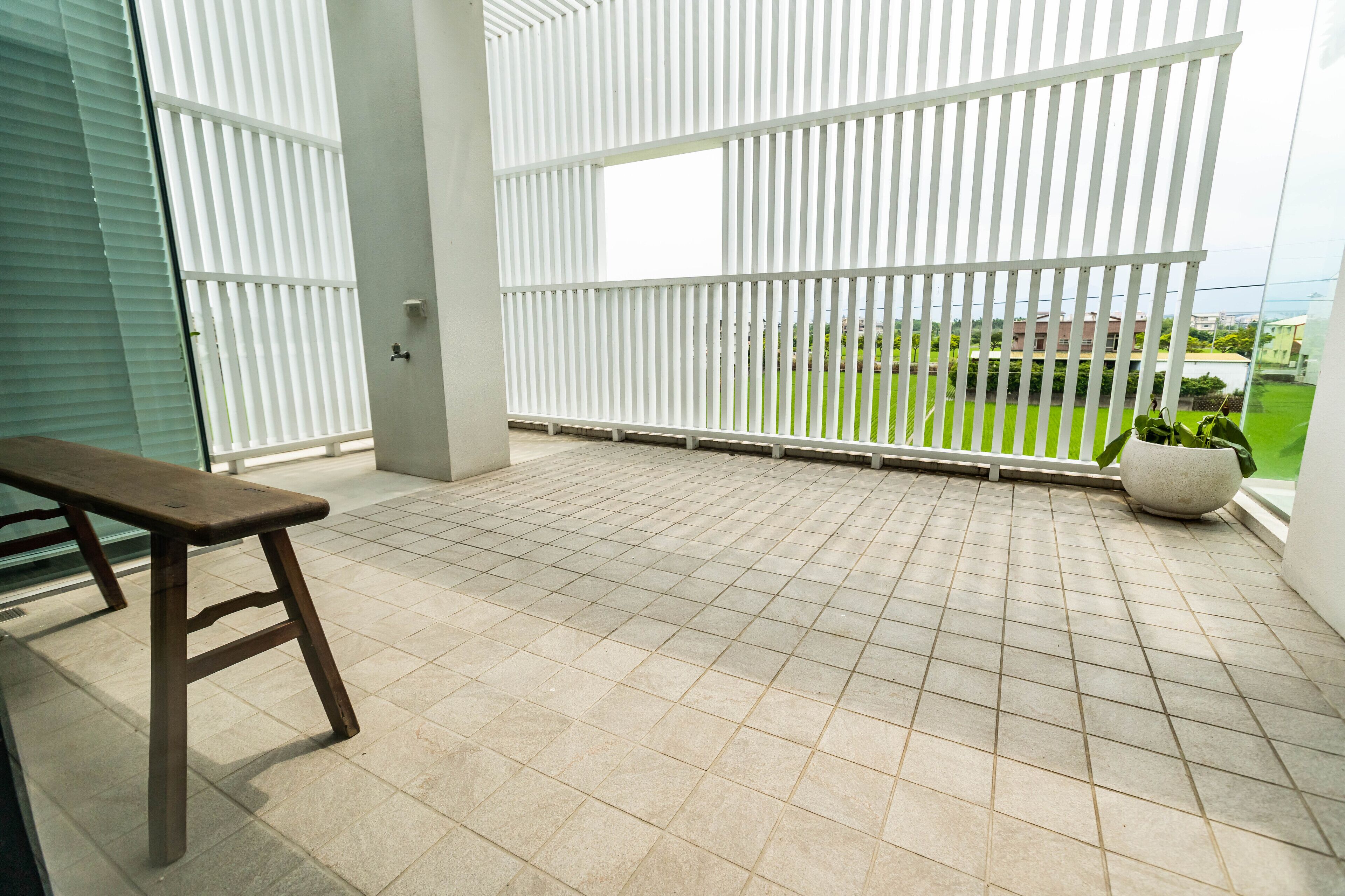 A balcony with a tiled floor, a wooden bench, and a potted plant.