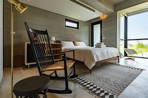Un dormitorio moderno con una cama, un sillón mecedora, un escritorio y un ventanal grande.