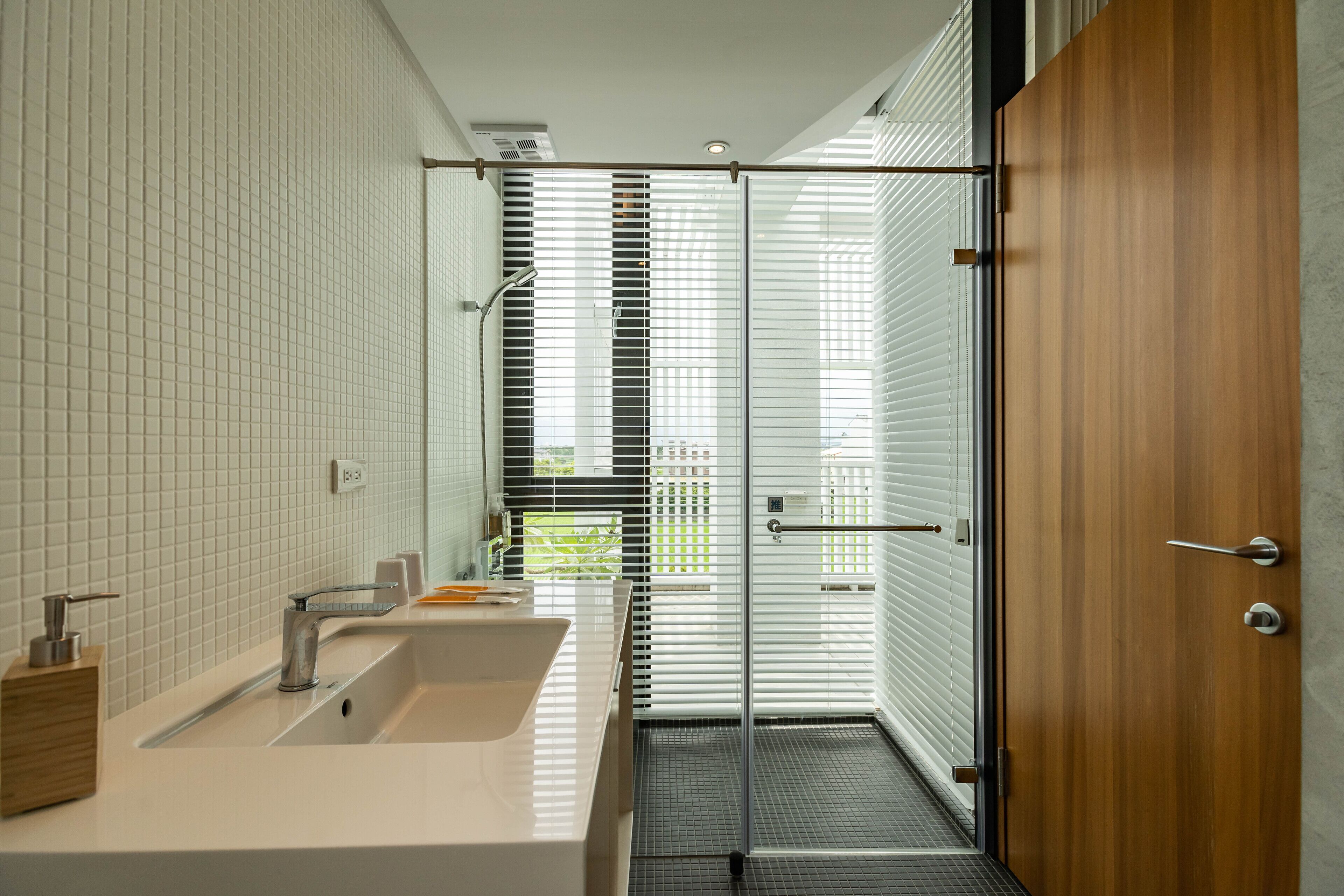 A modern bathroom with a large sink, a shower, and a glass door leading to a balcony.