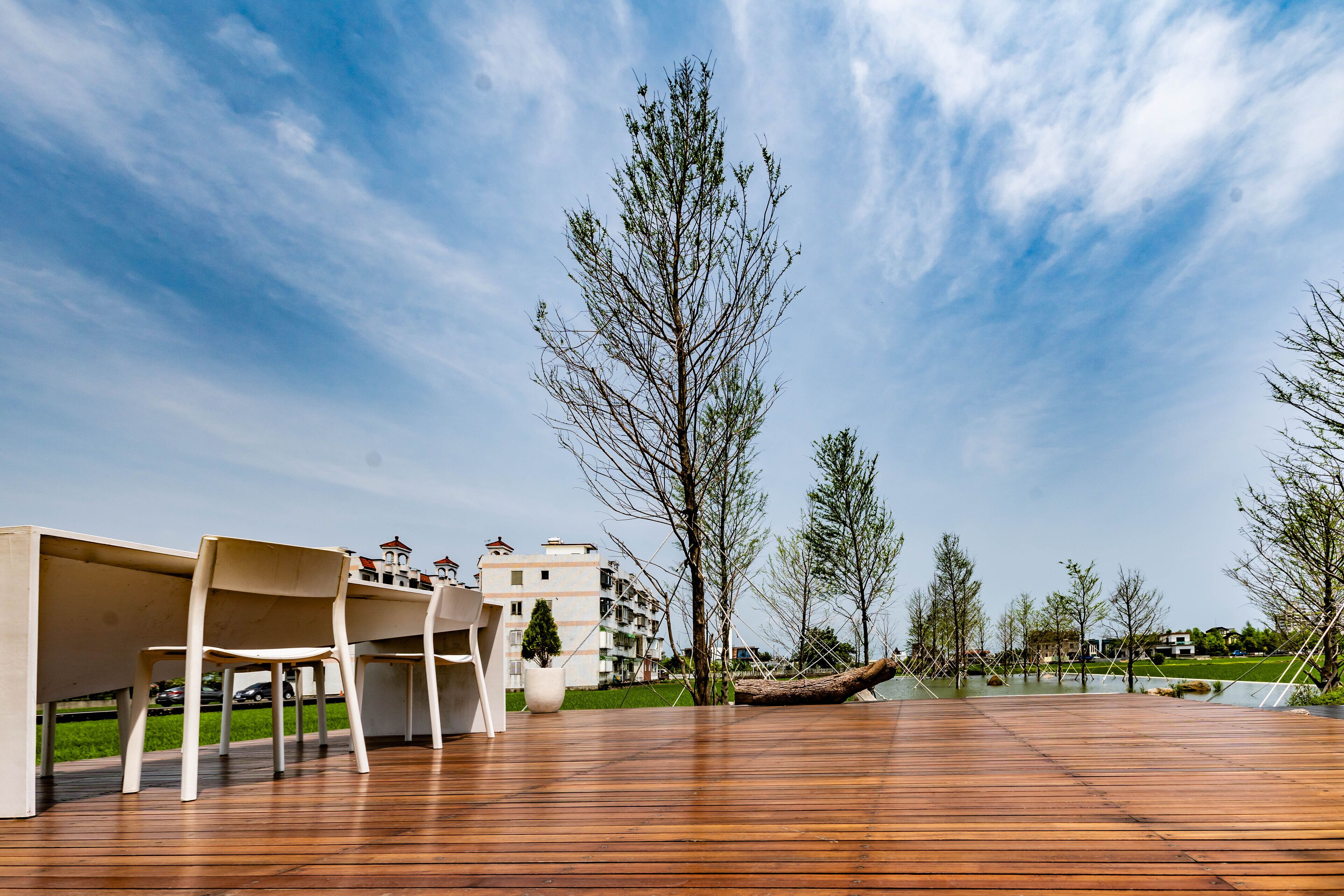 Una terraza de madera con sillas, una planta en maceta y una vista de un edificio al fondo.