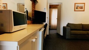 Un espacio habitable compacto con kitchenette, televisión de pantalla plana, sofá y puerta que da a otra habitación.