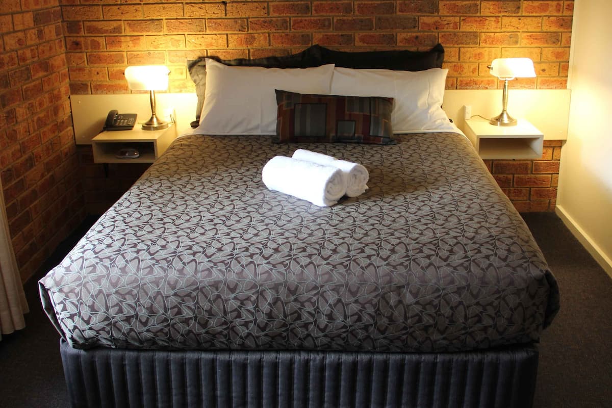 Una cama bien hecha con una colcha estampada, dos lámparas de noche y un teléfono en la mesita de noche.