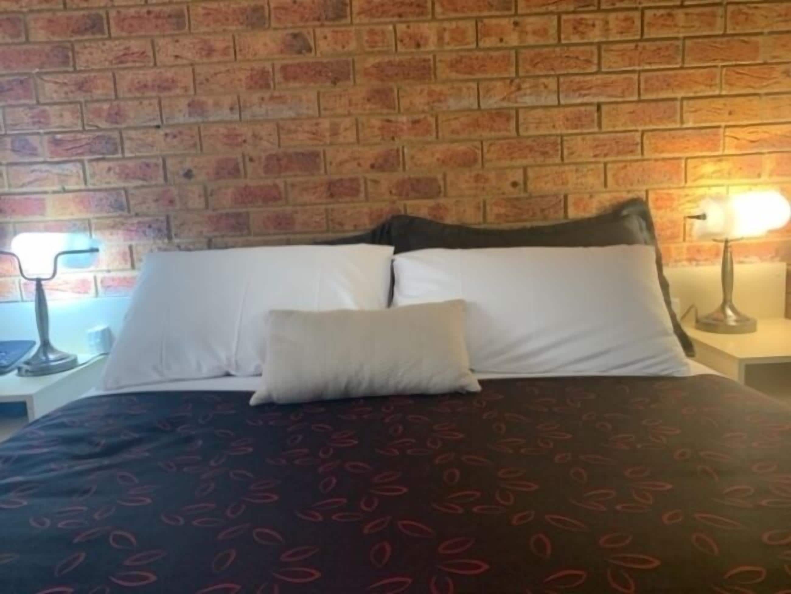 A bed with white pillows and a matching throw, a brick wall, and two bedside lamps.