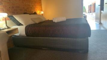 A hotel room with a brick wall, a bed with a patterned bedspread, a nightstand with a lamp, and a view of the street outside.