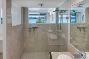 A modern bathroom with a glass shower enclosure, a large mirror, and a view of a lake. - Frangipani Lodge 002, Beachfront Apartment on Hamilton Island (Hamilton Island)