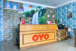Een hotel receptiebalie met een houten toonbank, een groot 'OYO' bord, ingelijste foto's aan de muur en een mural met een waterval.