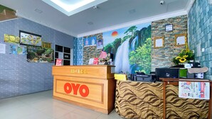 Ein Hotel-Rezeptionsbereich mit einem hölzernen Empfangstresen mit dem Aufdruck 'OYO', einem Wandgemälde eines Wasserfalls und verschiedenen Informationsplakaten an den Wänden.