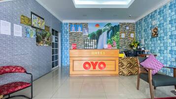 Una zona de recepción de hotel con un mostrador de madera identificado como 'HOTEL OYO', una pared de ladrillo azul y un gran mural de una cascada.