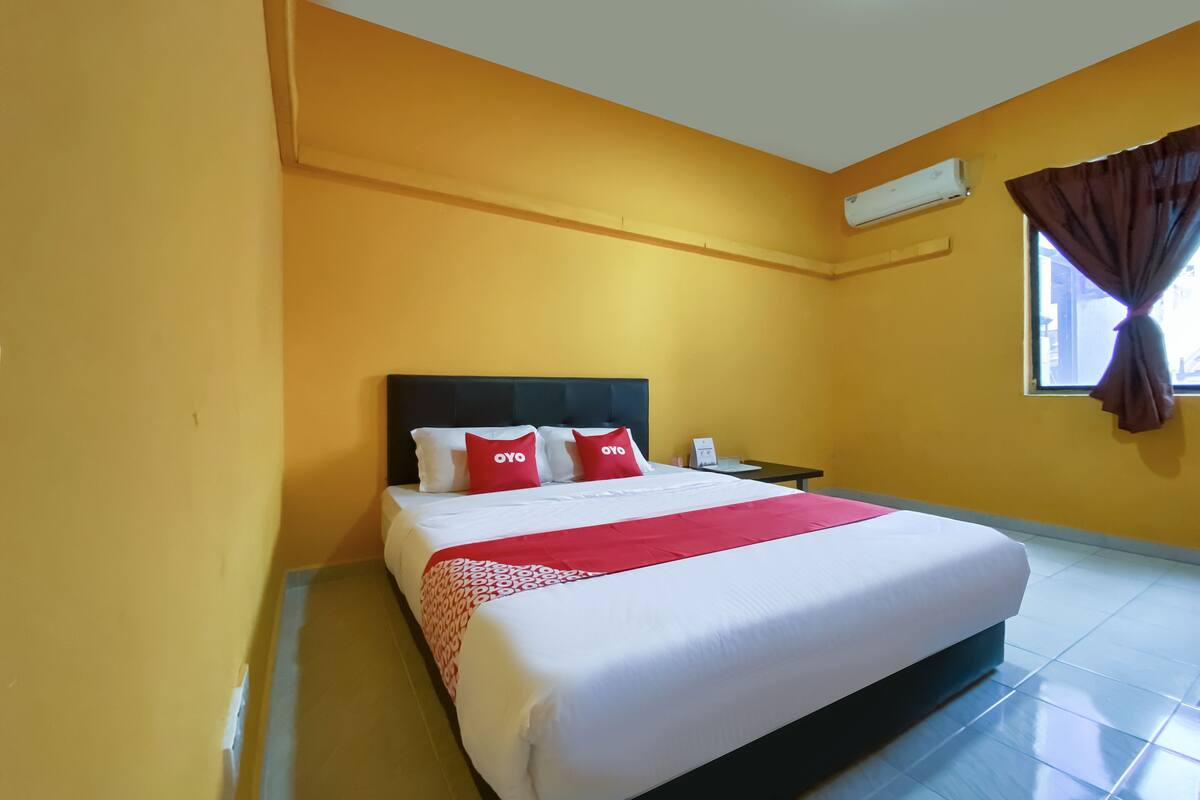 Een hotelkamer met een groot bed, nachtkastje, airconditioning en een raam met gordijnen.