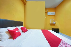 Een hotelkamer met een bed, twee rode kussens met 'OYO'-logo, een wit-rode spreideken, een zwart nachtkastje en een wandgemonteerde airconditioning.