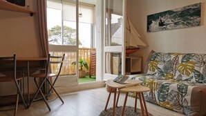 A living room with a sofa, a small table, and a TV on a shelf. - Nice renovated apartment at the beach, thalasso (Roscoff)