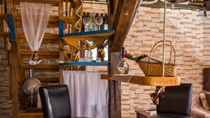 A rustic interior with wooden beams, a brick wall, and a hanging basket with bottles.
