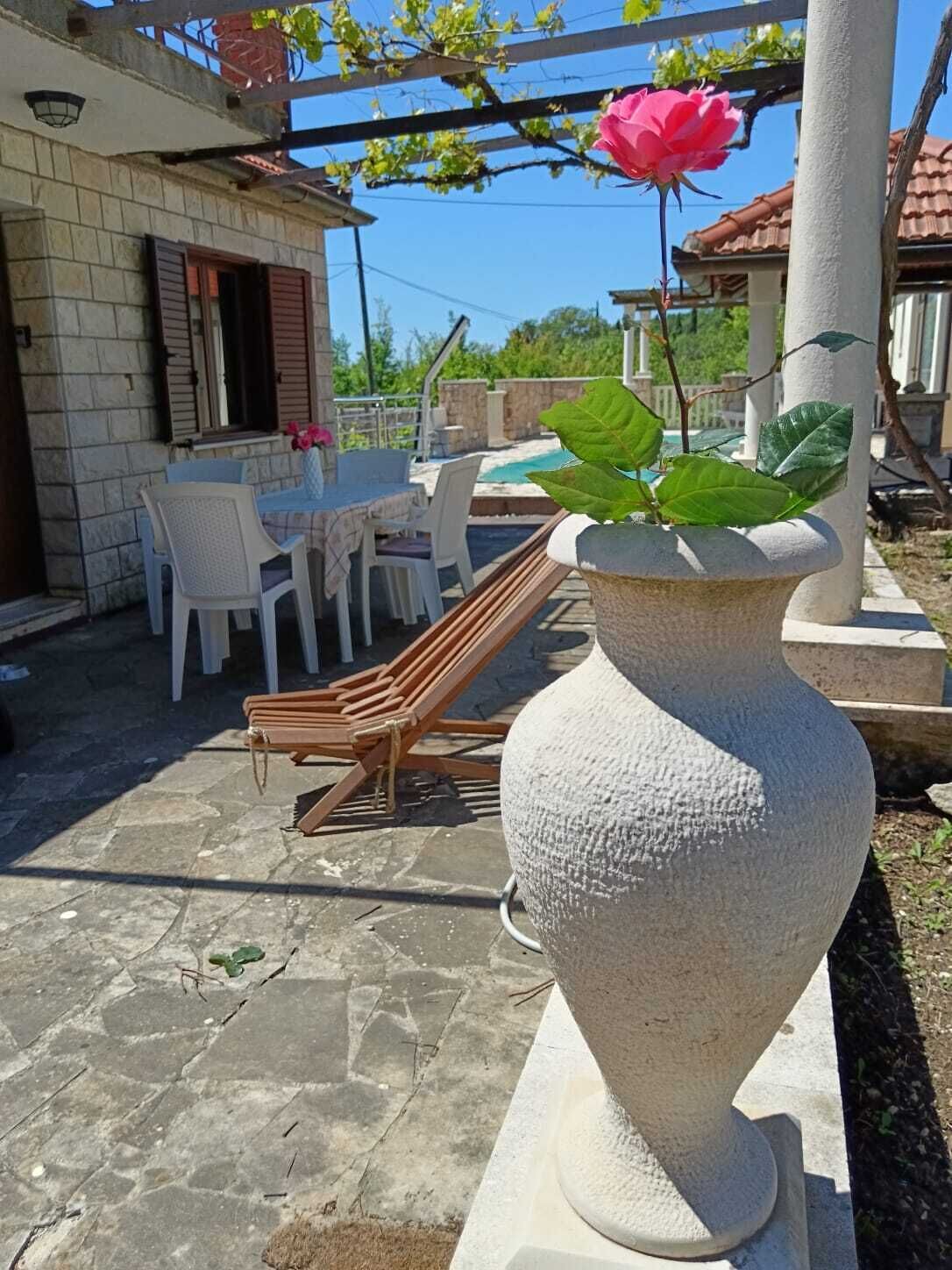 Una jardinera de piedra con rosales, mobiliario exterior y una piscina al fondo.