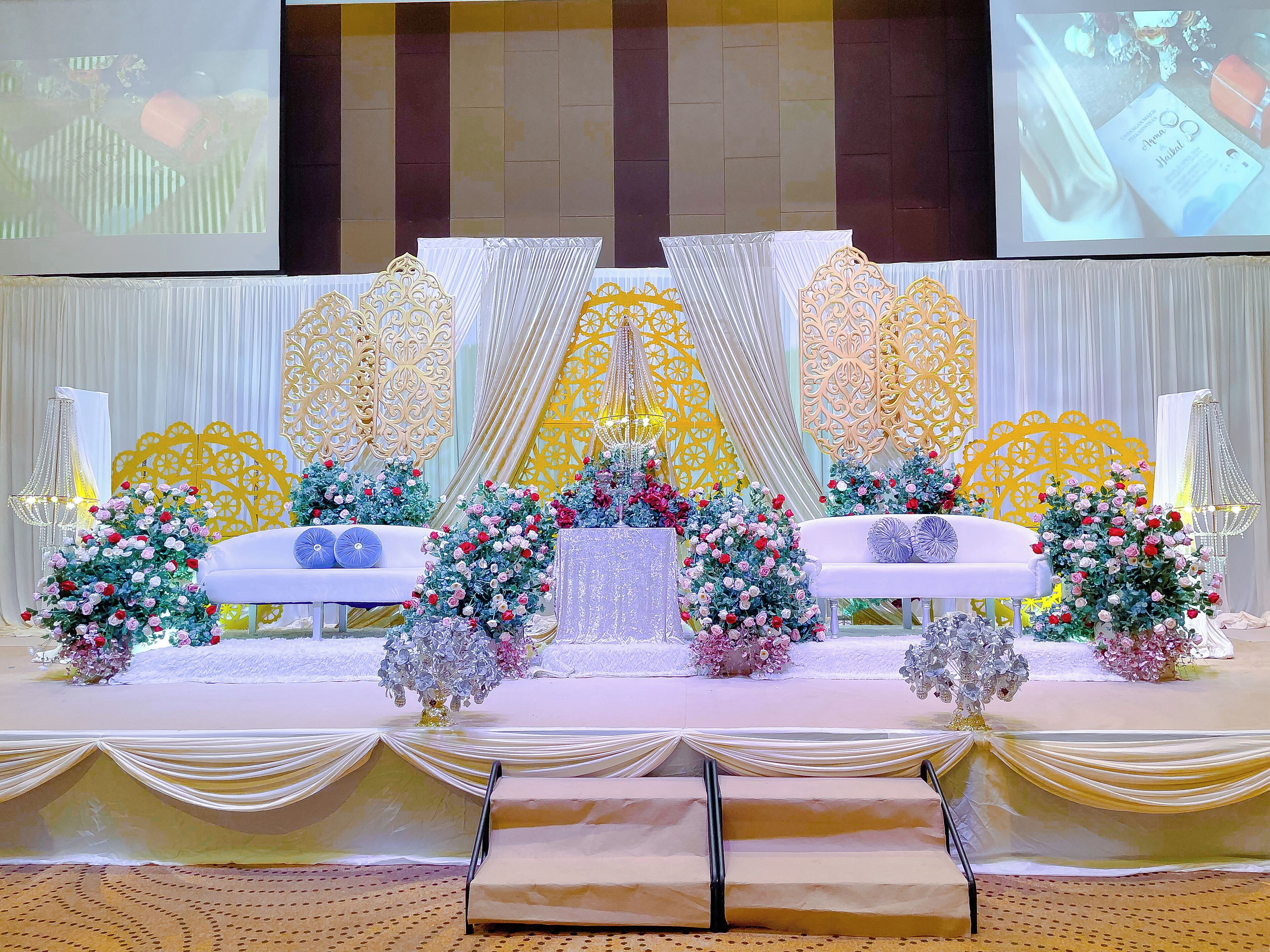 A stage with a white backdrop, golden decorative panels, and floral arrangements.