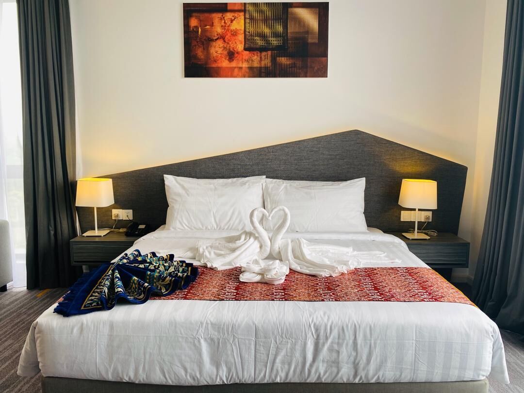 Ein Hotelzimmer mit einem großen Bett, zwei Nachttischlampen, einem Wandbild und einer roten und weißen Tagesdecke.
