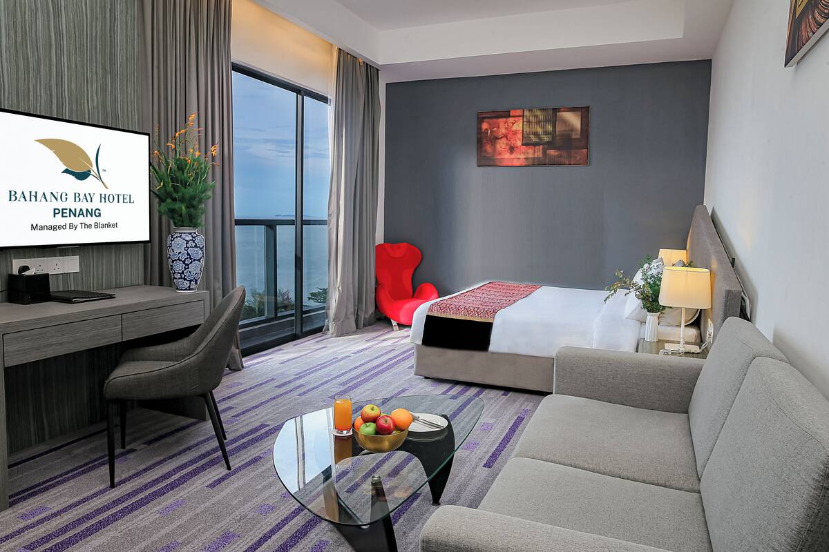 Une chambre d’hôtel équipée d’un lit, d’un canapé, d’un bureau et d’un téléviseur affichant le nom de l’hôtel.