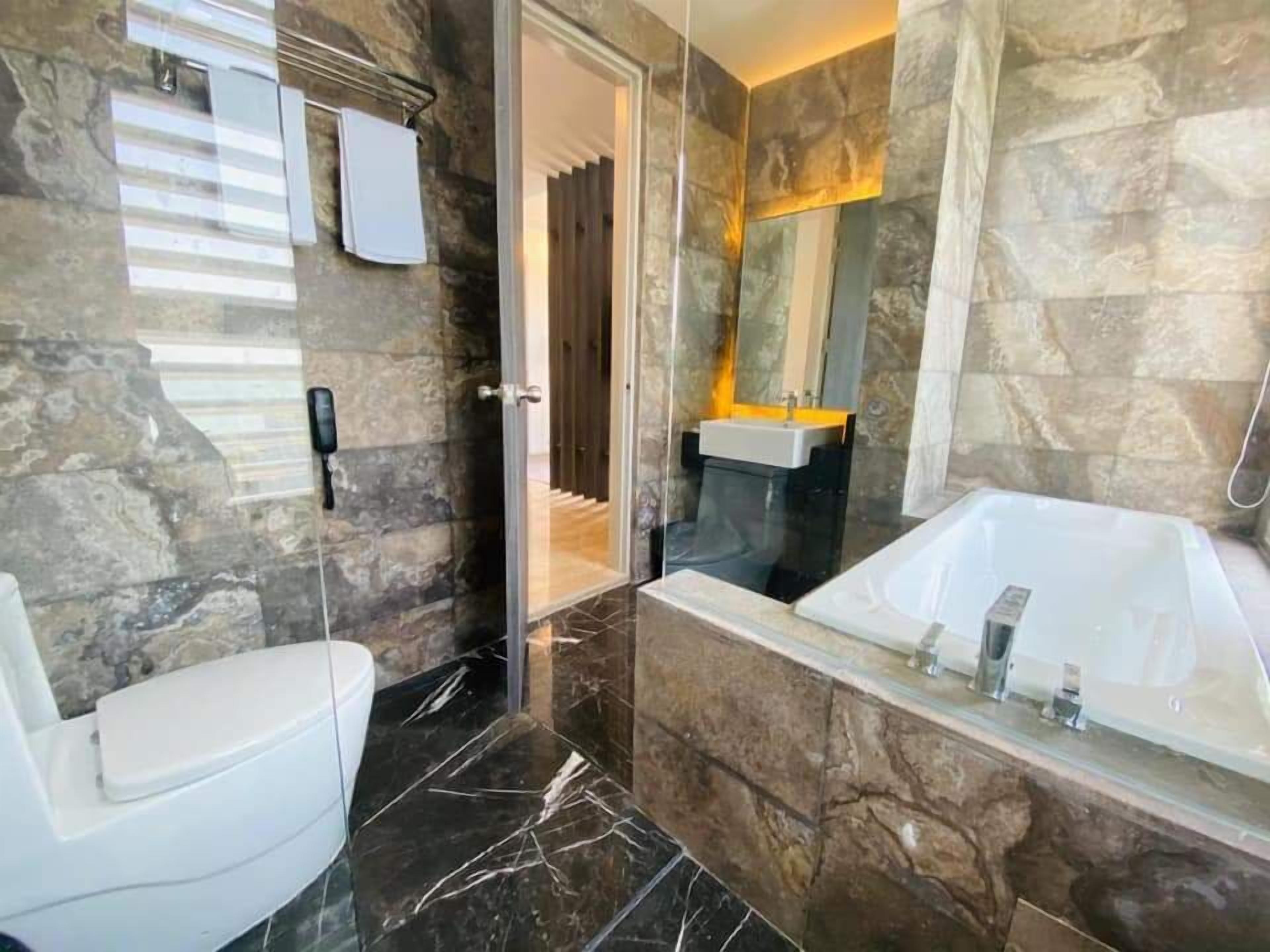 Un baño con piso de mármol, inodoro blanco, ducha con cerramiento de vidrio y una bañera grande.