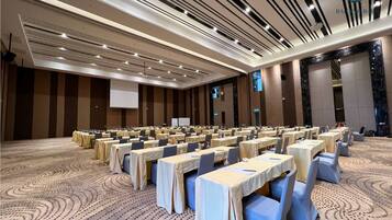 A large conference room with rows of tables and chairs, a projector screen, and a patterned carpet.